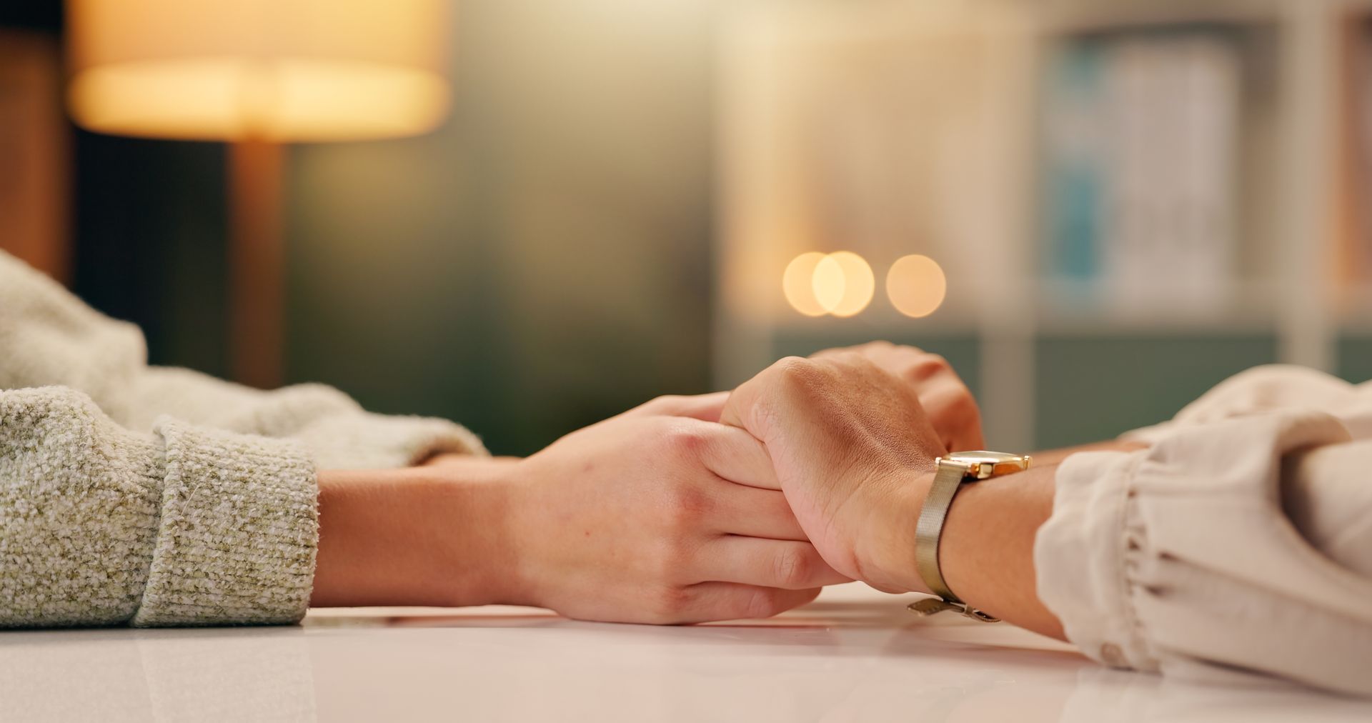 Two people holding hands across a table in a warm indoor setting