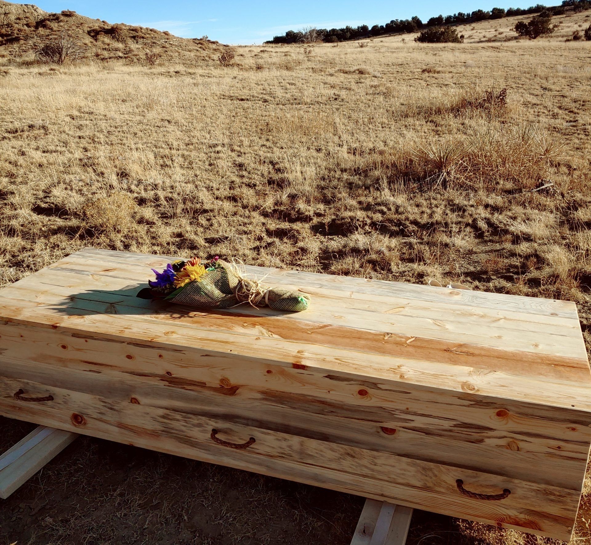 Wooden coffin on dry grassland with a small flower arrangement on top