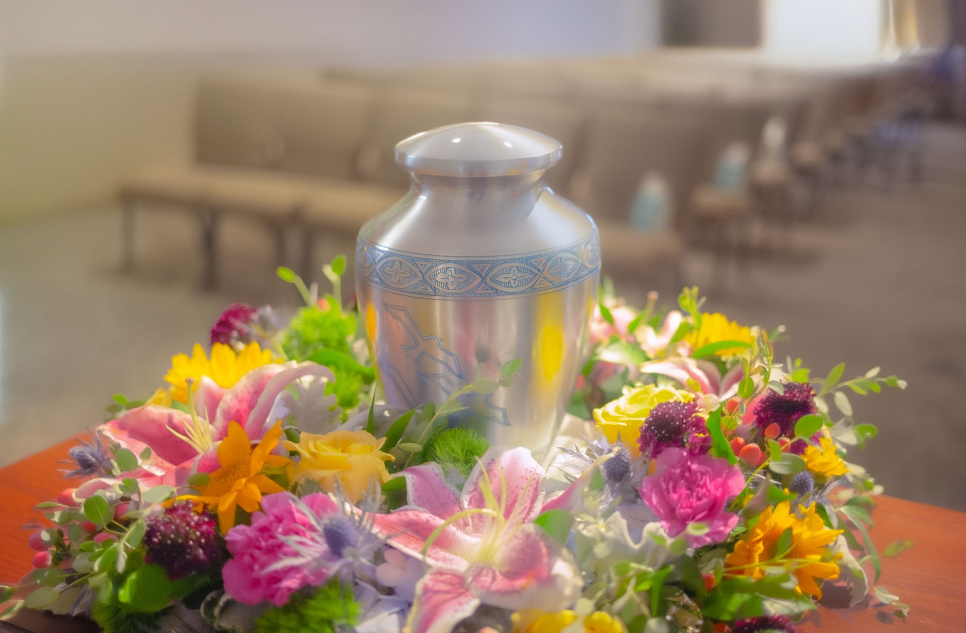Silver urn surrounded by colorful flowers on a table in a softly blurred room
