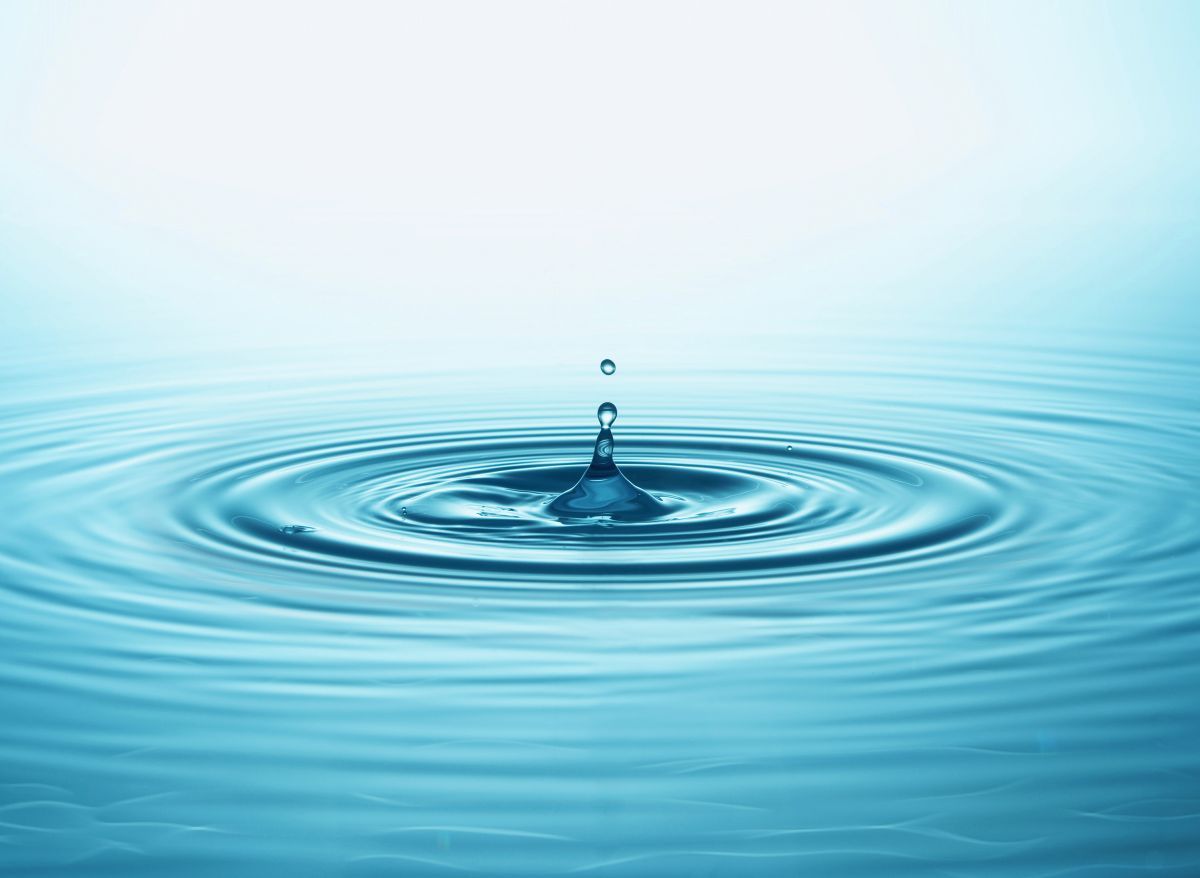 Blue water droplet splashing into calm ripples on a light aqua background