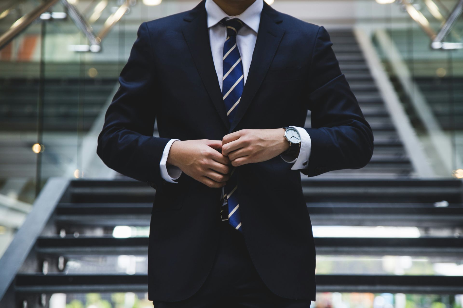 Businessperson adjusting tie in a dark suit on an indoor staircase.